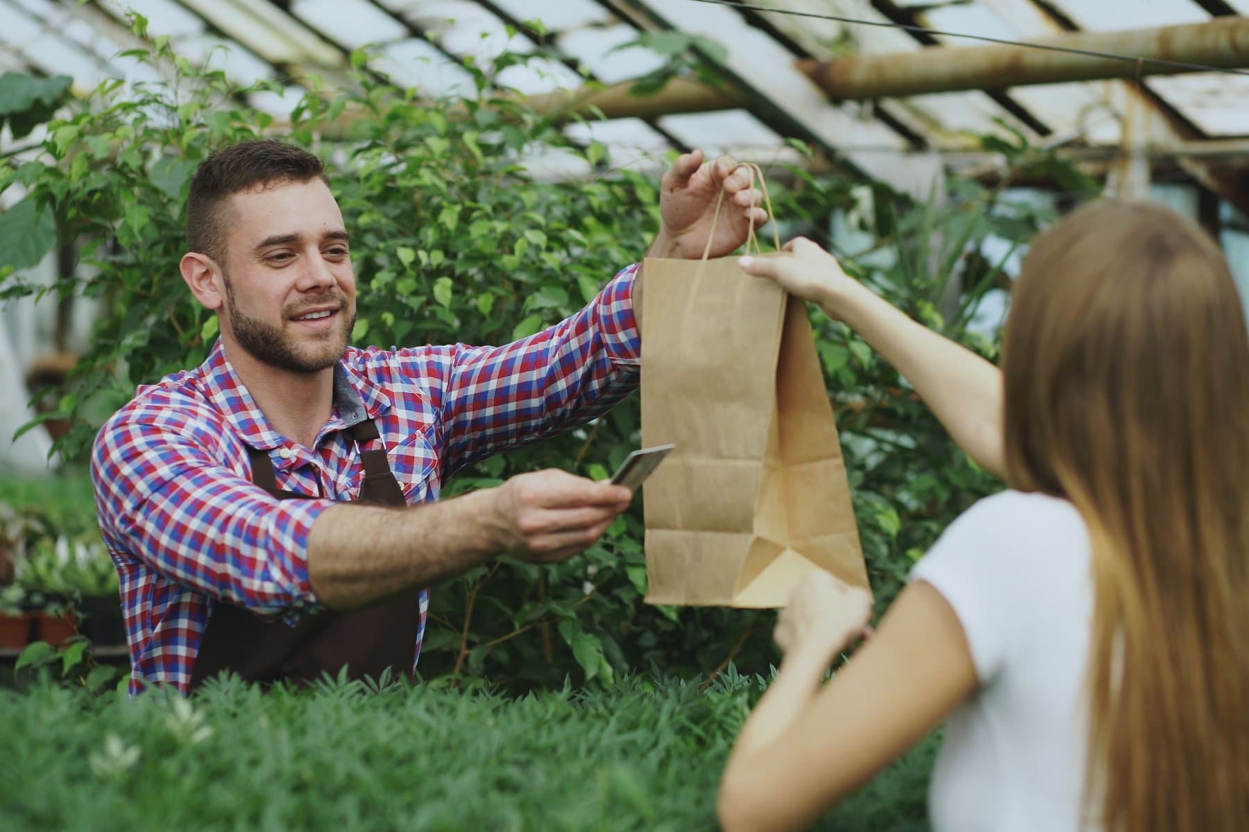 Greenhouse associate handing a customer a paper shopping bag while returning a card