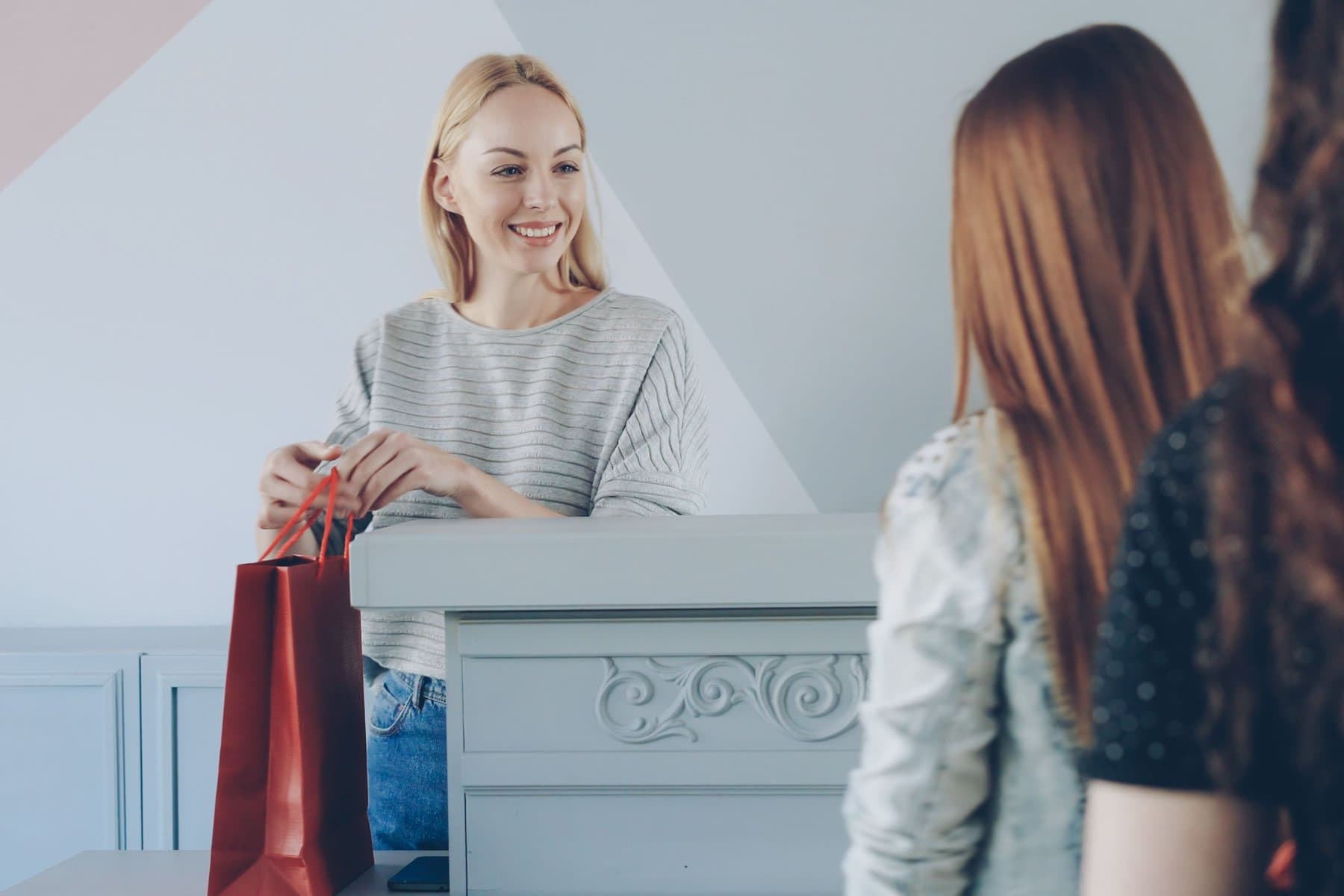 Store associate handing a red shopping bag to two customers at a specialty-retail counter