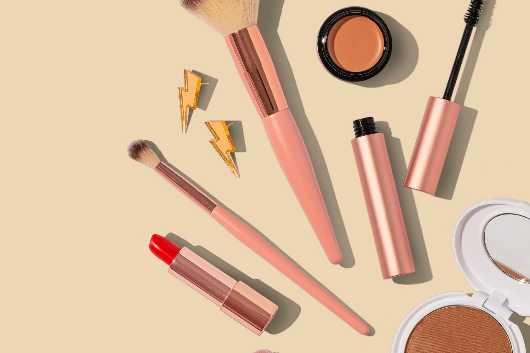 Unbranded makeup brushes, mascara, lipstick, blush, and compact arranged on a neutral surface