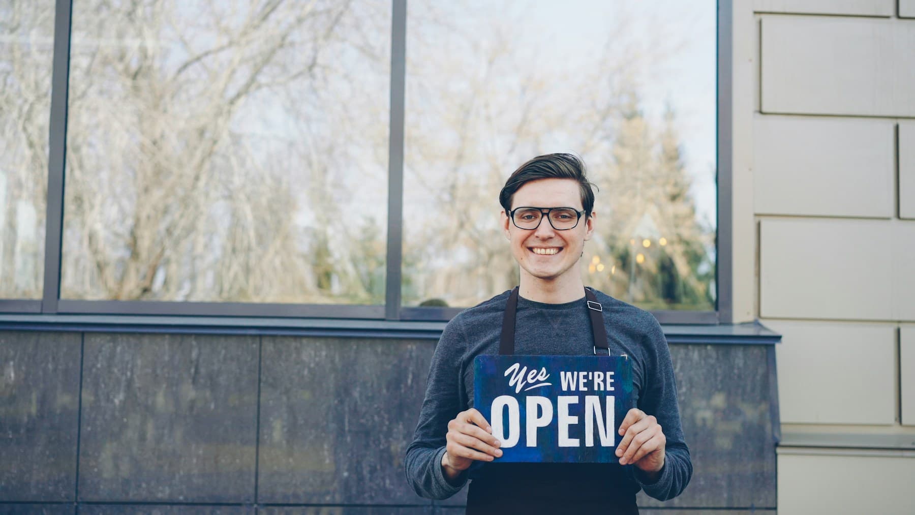 Store operator holding an open sign at a storefront entrance