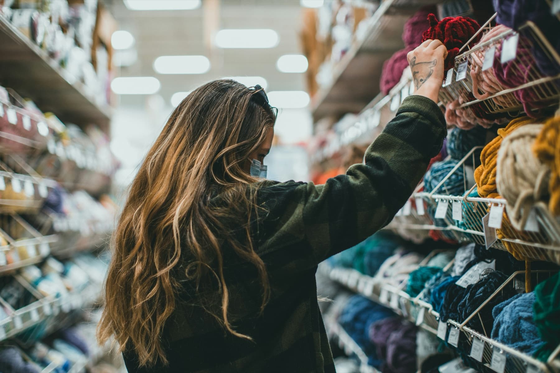 Shopper reaching for red yarn on a stocked craft-store shelf