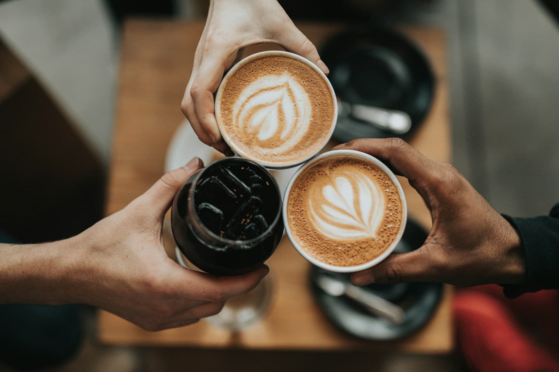 Three people holding coffee drinks together over a table